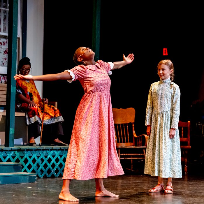 A girl in a coral dress, arms flung wide, beside a girl in a pale dress watching her