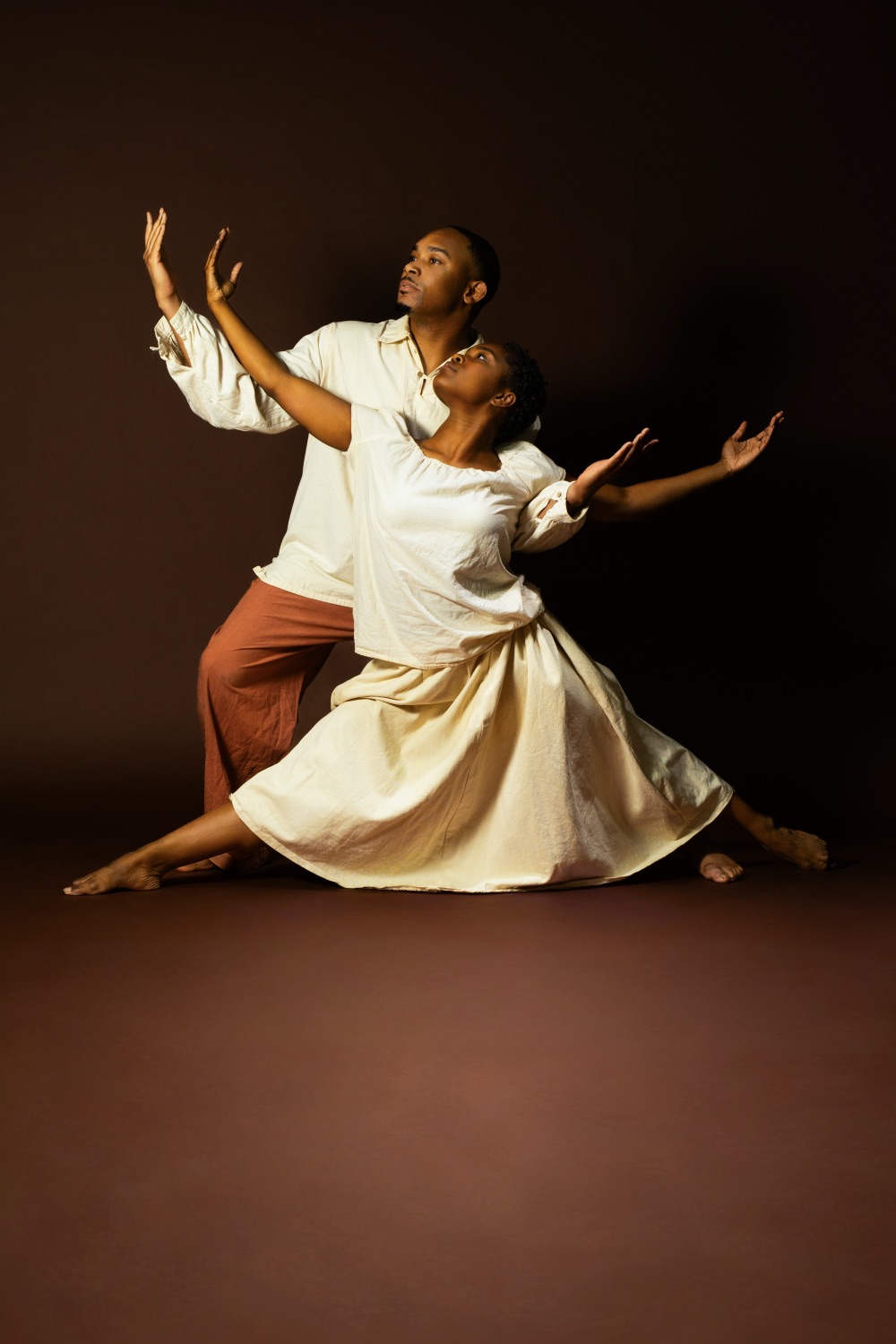 Two dancers in cream period dress soaring in a duet against a dark ground